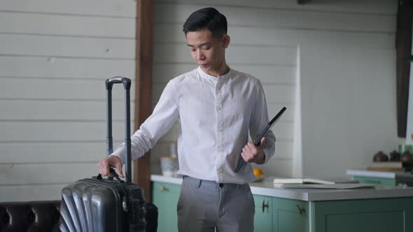 Thoughtful Young Asian Man Leaving in Slow Motion with Travel Bag and Tablet alt