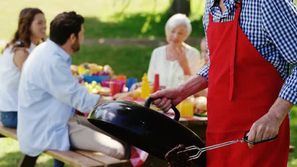Senior man preparing food on barbecue in the park alt