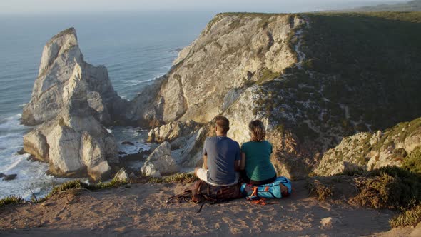 Couple of Backpack Tourists Sitting at Cliff alt