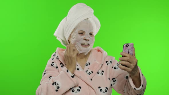 Grandmother in Bathrobe, Face Mask. Old Woman Making Selfies Using Mobile Phone alt
