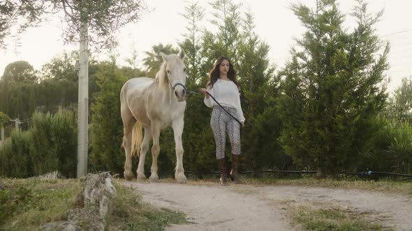 Woman Walks in the Dirt Road with White Horse alt