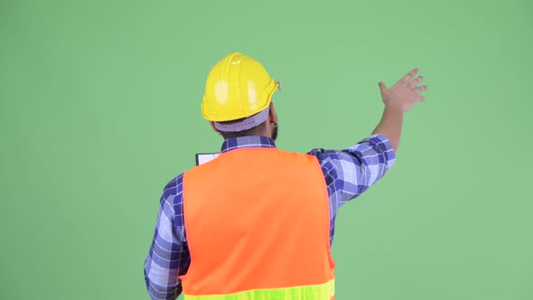 Rear View of Young Overweight Bearded Indian Man Construction Worker Pointing Finger alt