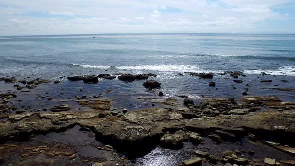 Side view tracking shot of a young man running on a rocky ocean beach shoreline. alt