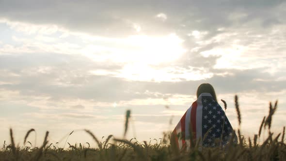 Patriotic Young Woman Stands in a Field Wrapped in the US Flag alt