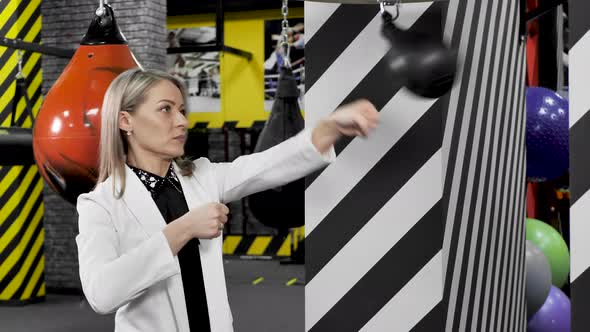 Serious Focused Businesswoman Hits a Punching Bag in the Gym