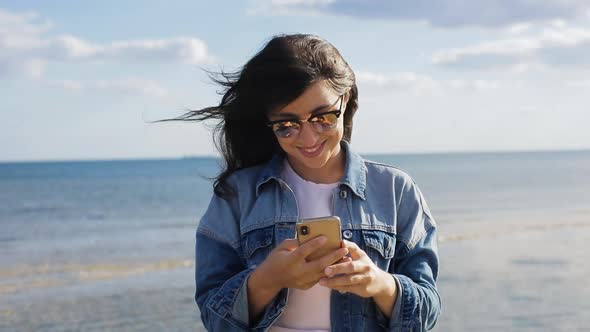 Attractive Brunette Woman in Jeans Jacket and Sunglasses Chat By Mobile Phone with Friends at Tha
