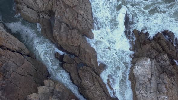 Aerial view over waves breaking onto rocks in the ocean alt