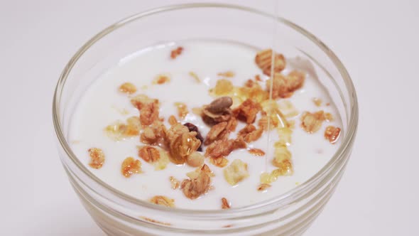 Person Pours Honey on Yogurt with Granola Close Up. The Main Components of a Delicious and Healthy