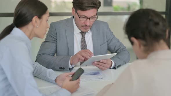 Middle Aged Businessman using Tablet and Female Colleague using Smartphone alt