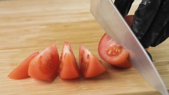Cook's Hands in Black Gloves Cutting Fresh Tomato Into Pieces on Wooden Board