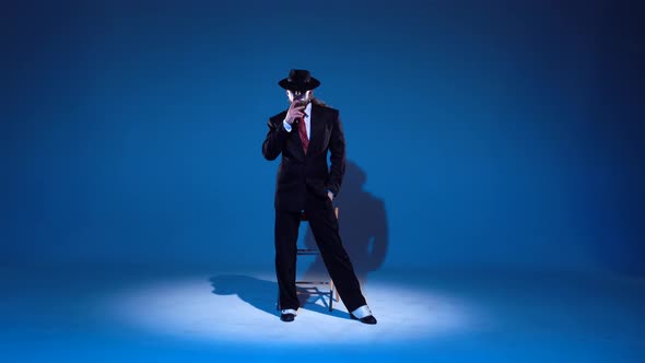 Elegant Man in a Black Hat Is Dancing an Erotic Dance, Spotlight on a Blue Background alt