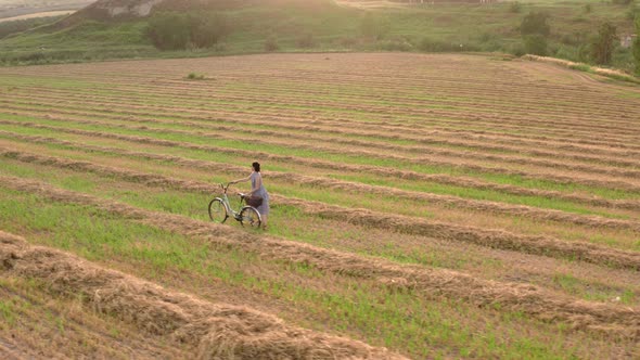 Girl Rides a Bicycle on a Rural Field in the Evening Before a Sunny Sunset,  Rows of Harvested Wheat alt