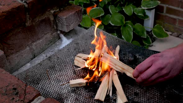 Man stokes small fire using kindling alt