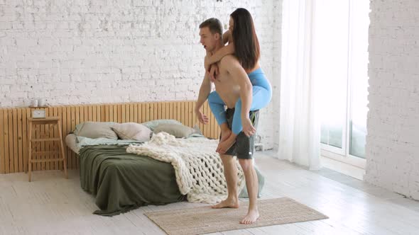 Man Is Doing Squat Exercise with Woman on His Back Instead of Barbell at Home