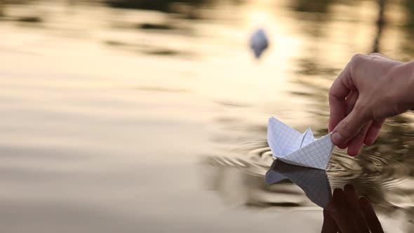 Close-up a child's hand puts a paper boat in the water. Dreams future childhood freedom hope concept