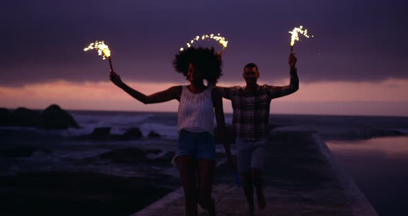Couple running with sparklers on concrete pier at beach 4k