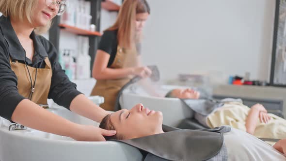 Group of young woman lying down on salon washing bed getting hair washed by hairdresser in salon. alt