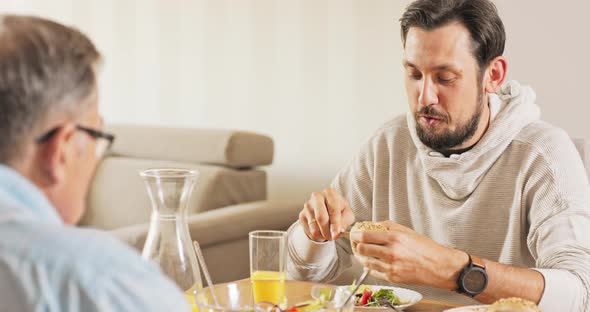 A Handsome Young Brunet Sits with His Father at the Table They Eat Breakfast Together alt