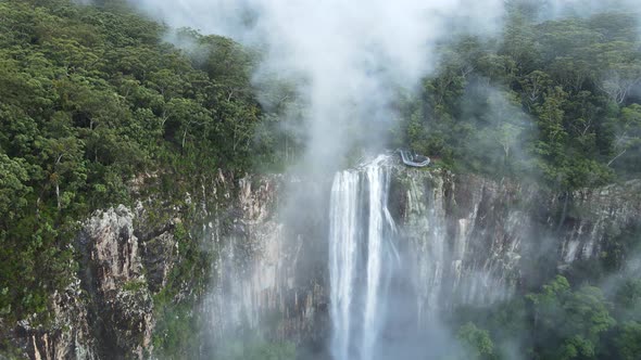 Cinematic view flying through fog clouds to reveal a majestic waterfall flowing into a tropical rain alt