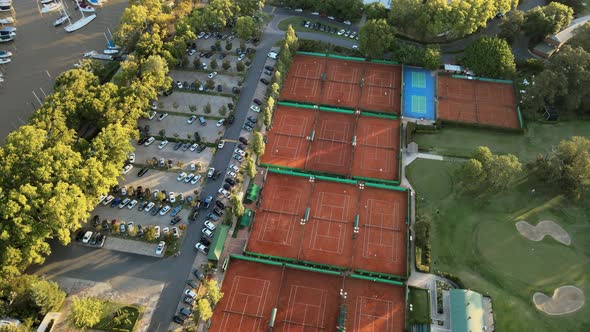 Aerial orbiting over clay tennis courts, a golf playground and a parking lot on a private sport club alt