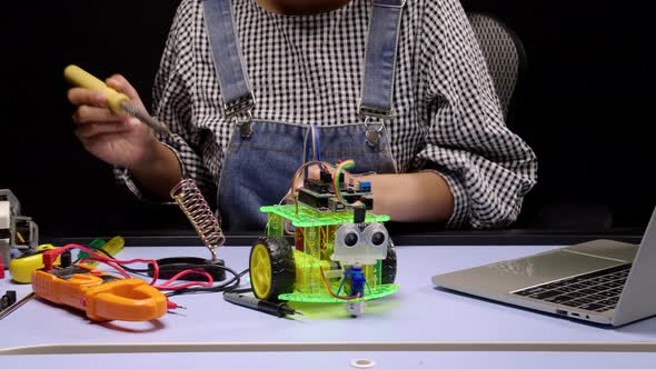 Robotics Engineers or student soldering the chip of PCB on robot cars. alt