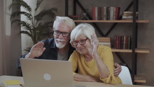 Senior Couple Sitting at Table and Using Laptop During Video Call at Home alt