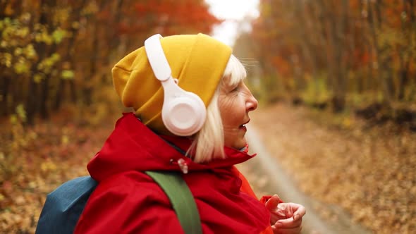 Happy 40s Woman in Colorful Yellow Clothing Putting on Wireless Headphones Listen Music While