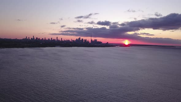 Aerial view across Lake Ontario of Toronto's skyline at dawn. alt