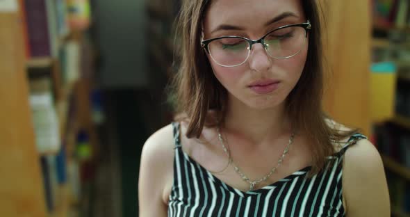 Girl in Glasses and Teeth Braces Reads a Book Then Looks and Smiles at Camera alt