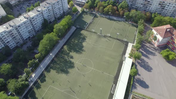 Aerial Shot of a City with a Soccer Field and Living Houses with Tall Trees alt
