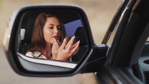 Reflection of Girl in Car Rear View Mirror Who Applying a Lip Gloss and Smiling alt