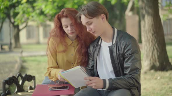 Middle Shot Portrait of Young Caucasian Man and Woman Sitting on Campus and Talking. Happy College alt