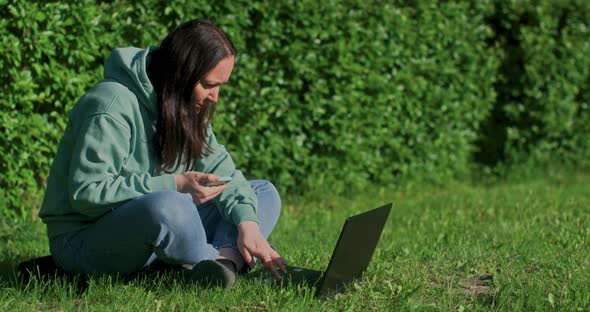 Woman is Working in Park Sitting on Grass Using Laptop Smartphone with Internet