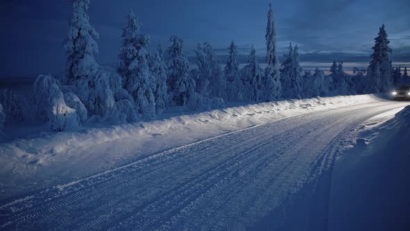 A Car With The Headlights On Travelling In The Snow Covered Road At Night In Lapland Region alt