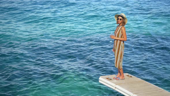 A woman with a glass of white wine on a dock over the Mediterranean Sea in Italy, Europe alt