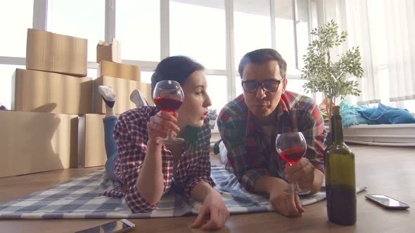 Young Couple Lies on the Floor Drinking Wine and Notes Moving Into a New Apartment alt