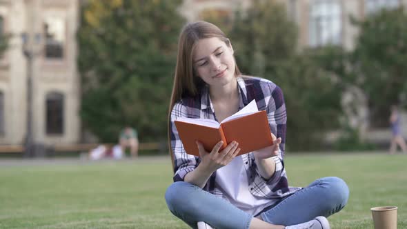 Young Woman Sitting on The Grass and Reading Book