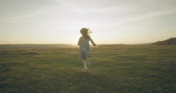 A Little Girl Is Running Through the Autumn Field Against the Background of the Sun alt