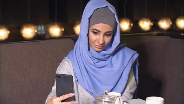 Beautiful Muslim Girl Using Smartphone in Cafe. Modern Muslim Woman and New Technologies
