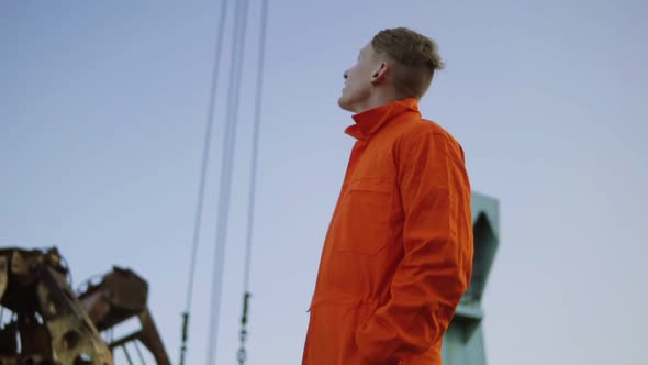Handsome Young Container Warehouse Worker in Orange Uniform Standing By the Ship at the Harbor and alt