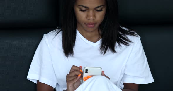Black woman using mobile phone lying on bed. alt