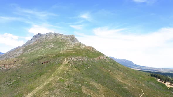 Aerial drone rotating around green mountain peak with forest and mountain range in background, summe alt
