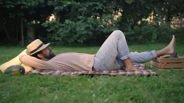 Side View of Young Male Farmer Sleeping Lying on Green Meadow with Harvest alt