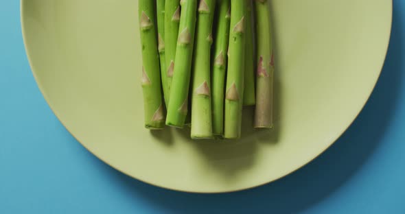 Video of fresh asparagus on green plate over blue background alt
