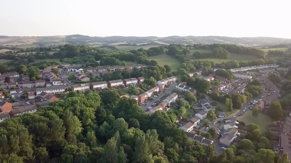 Aerial pull back of residential area surrounded by trees in Exeter, UK at sunset alt
