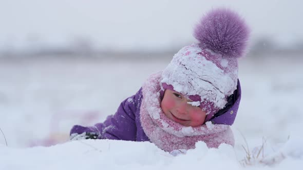 happy little girl in outerwear hat and scarf lies on the snow