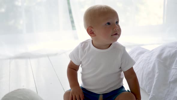 Child in a White T-shirt Sitting on the Floor in a White Room alt