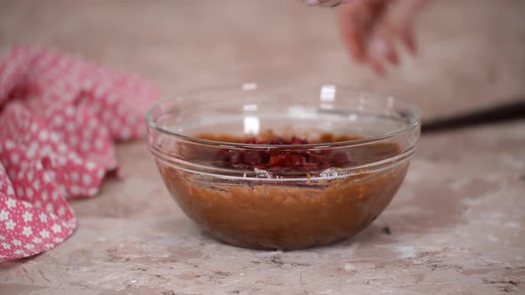 Female hands adding cherries to the chocolate batter, making delicious homemade brownie.