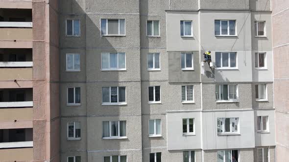 An Industrial Climber Suspended on Ropes and Paints the Wall of a Building with a Roller