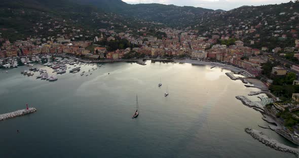 Golden hour aerial of tourist resort's colorful houses and packed marina, Italy alt